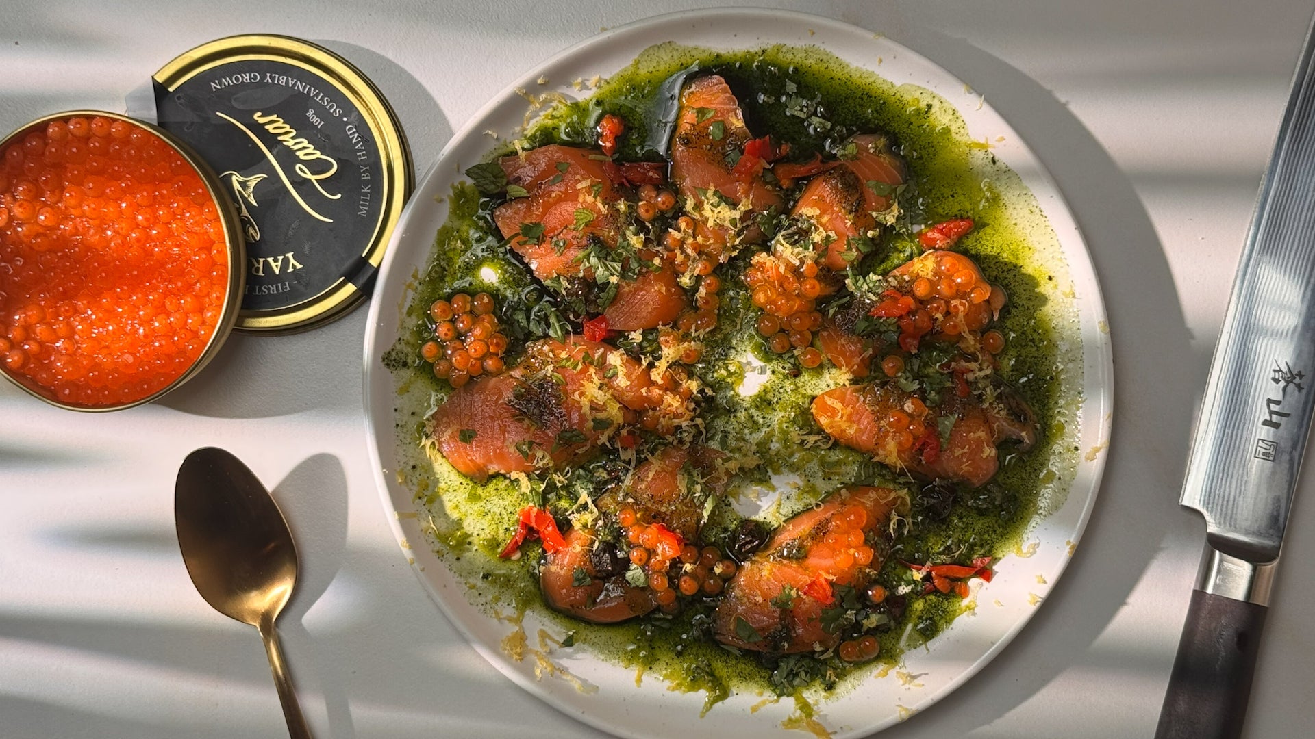 Plate of Seatopia Steelhead Plankton Marino Crudo garnished with cilantro leaves, lemon zest, and plankton sauce, next to a container of caviar.