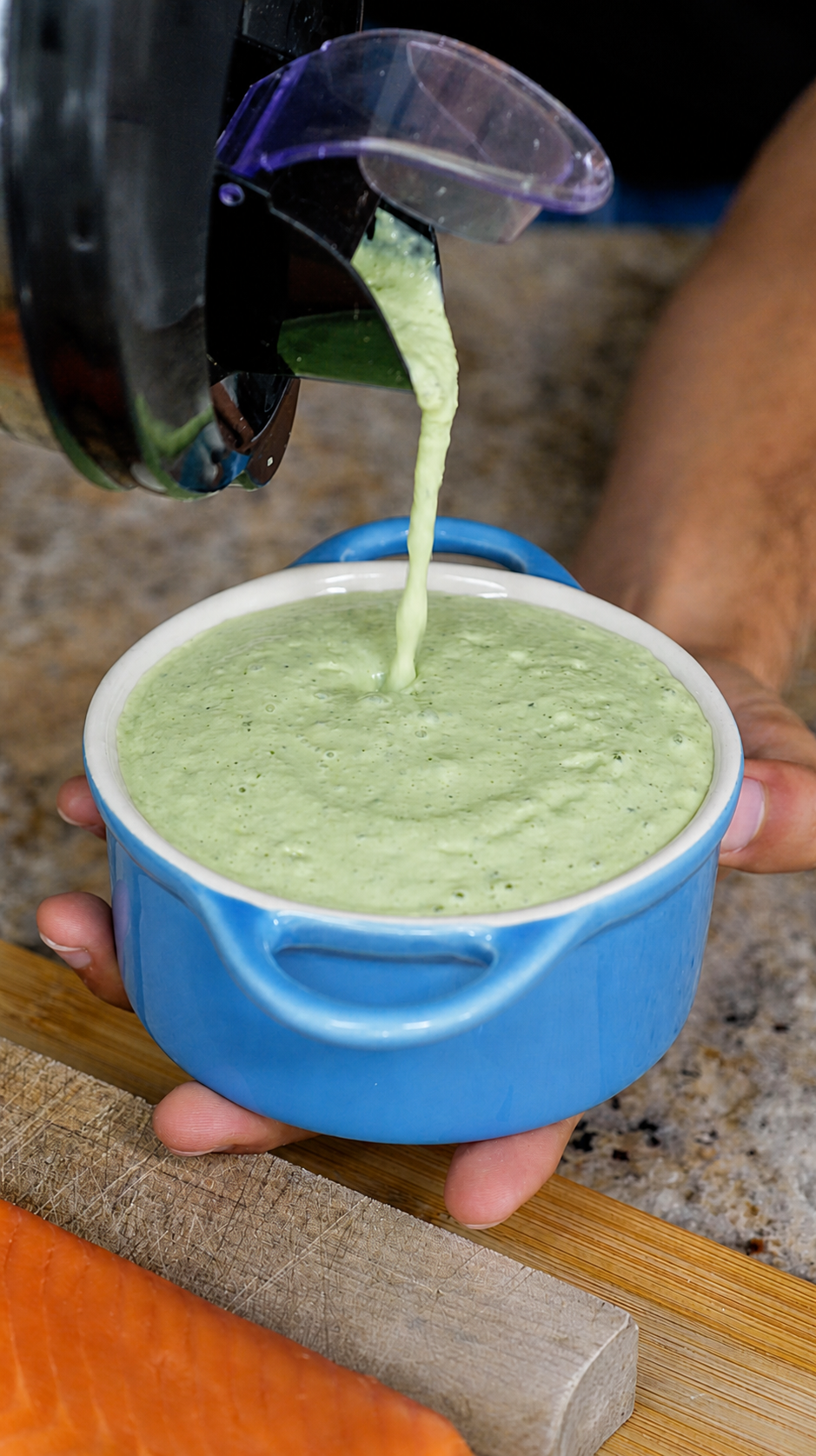 Green goddess tzatziki pouring from a blender into a blue dish, steelhead fillet on the board below