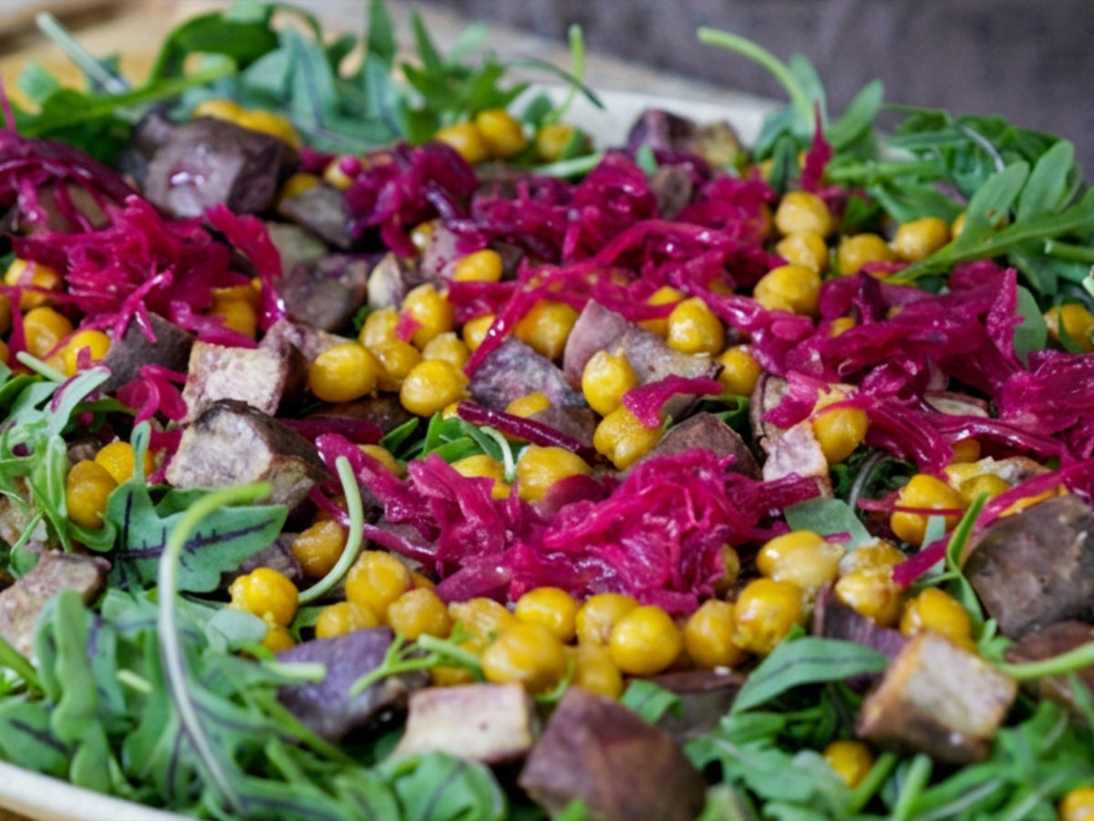 The salad base on a platter: wild arugula layered with roasted Okinawan sweet potato, crispy chickpeas, purple sauerkraut and broccoli sprouts