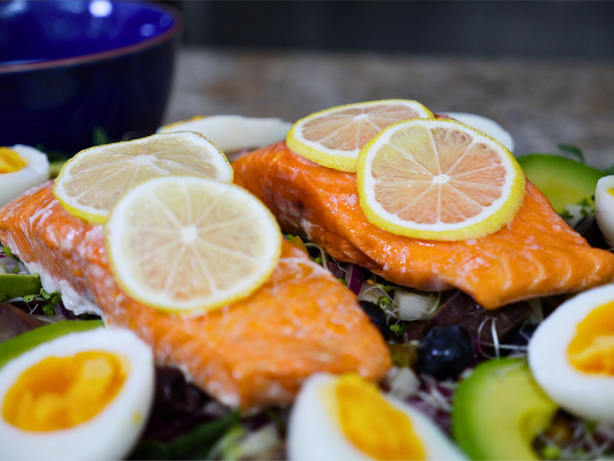 Close-up of two baked Seatopia salmon fillets topped with thin lemon rounds, resting on the salad