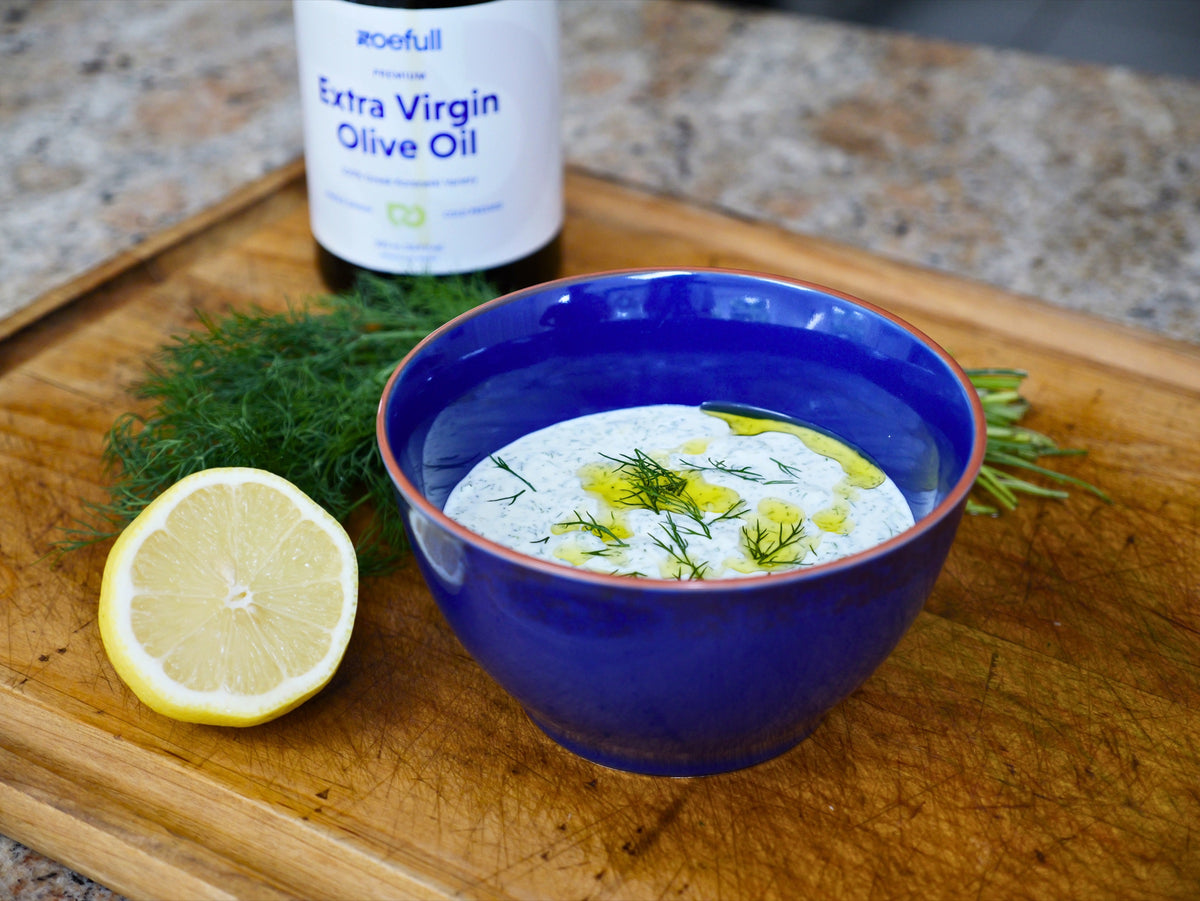 Honeyed dill tzatziki in a blue bowl, drizzled with olive oil, beside fresh dill and a halved lemon