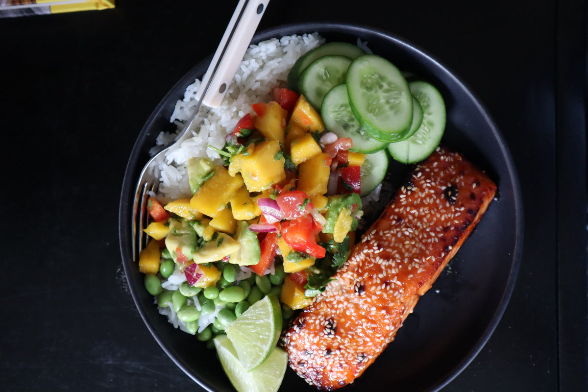 Overhead view of a hot honey salmon bowl with coconut rice, mango salsa, edamame, cucumber and lime