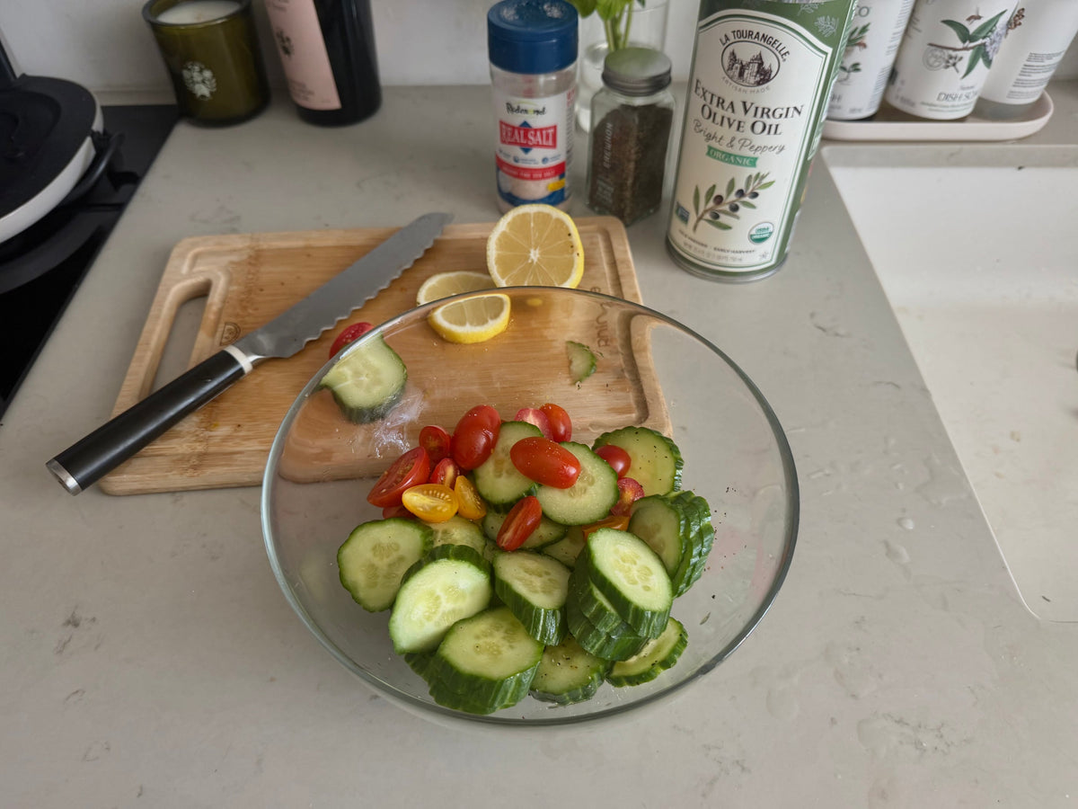 Sliced Persian cucumber and halved cherry tomatoes tossed in a glass bowl with olive oil, lemon, sea salt, and black pepper
