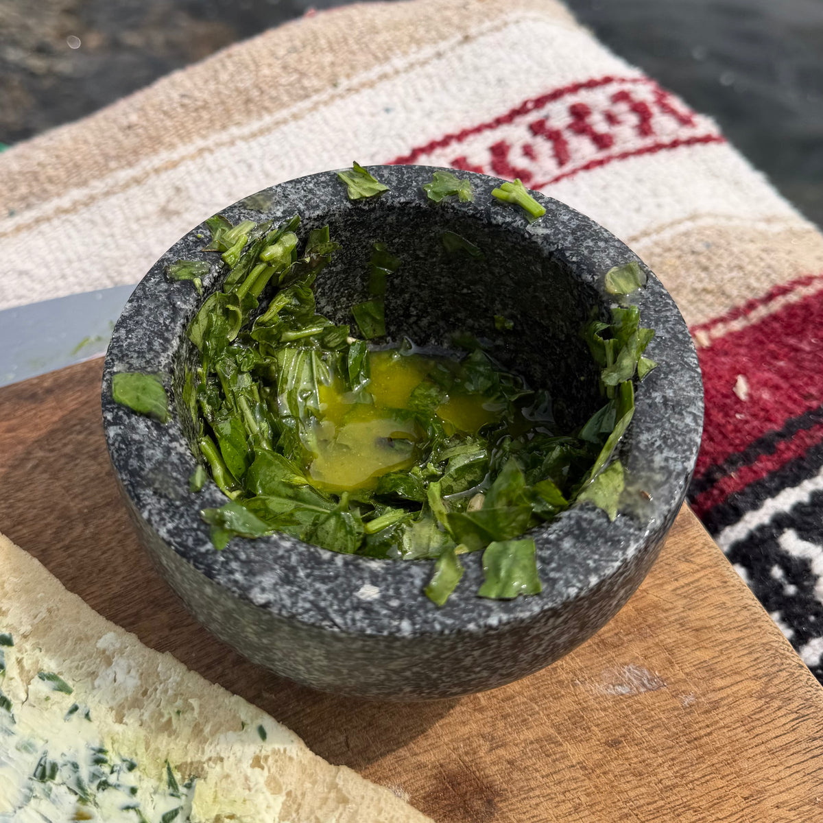 Fresh basil being mashed with olive oil and lemon in a stone mortar and pestle
