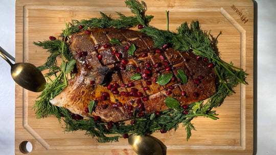 Cured Fish Ham displayed on a wooden cutting board, resting on a bed of fresh dill and garnished with mint leaves and pomegranate seeds, ready to serve.