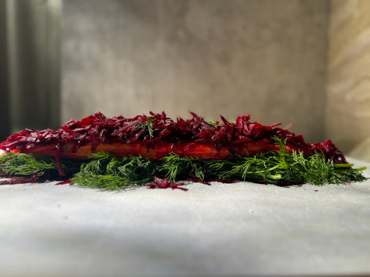 Beet-cured steelhead lox on a wooden cutting board, garnished with fresh dill and lemon zest.