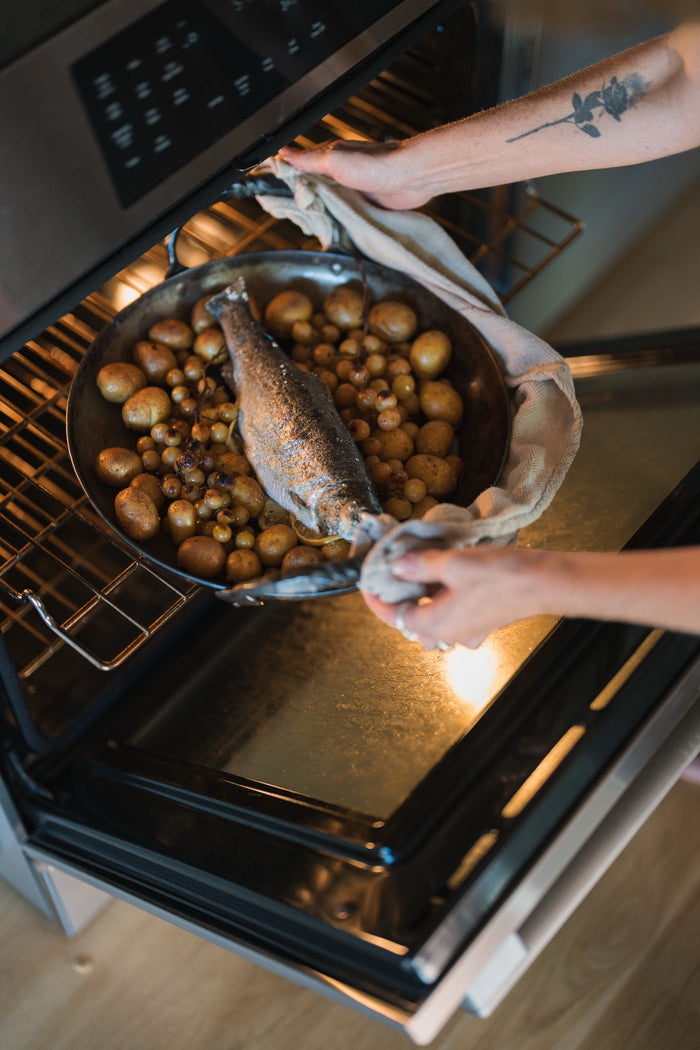 A sheet pan of whole roasted trout with potatoes and grapes being lifted from the oven