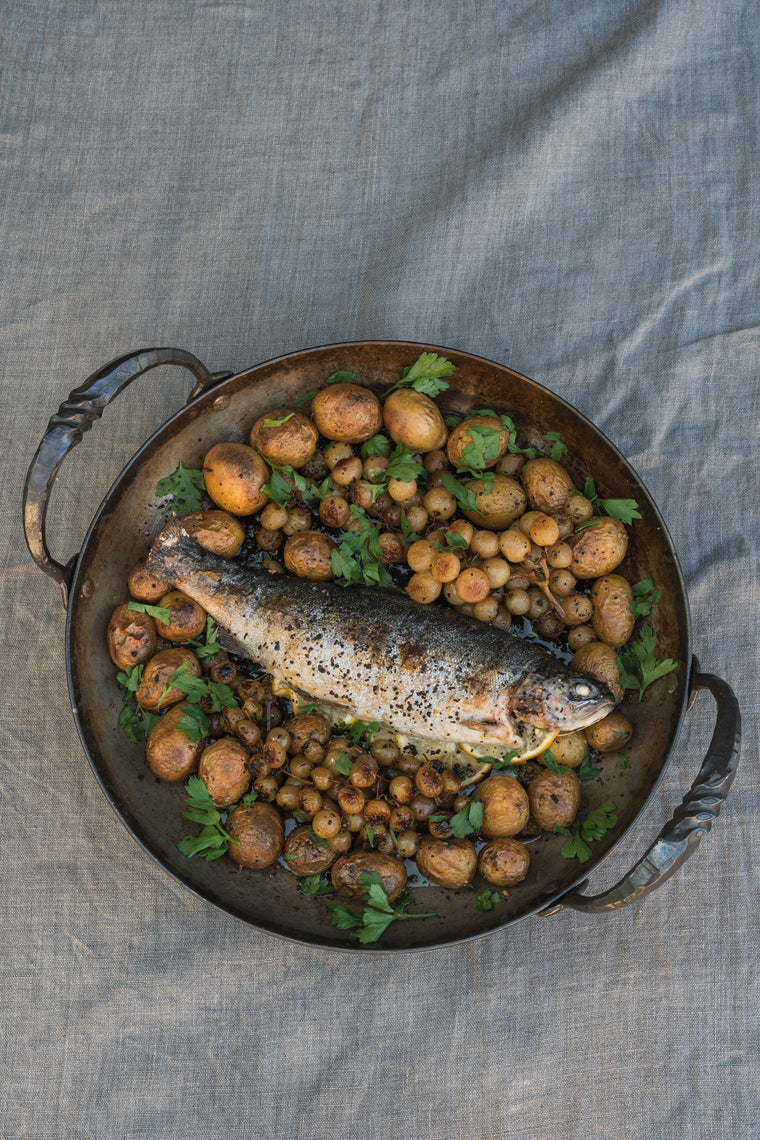Whole roasted trout on a platter with potatoes and blistered grapes, seen from above