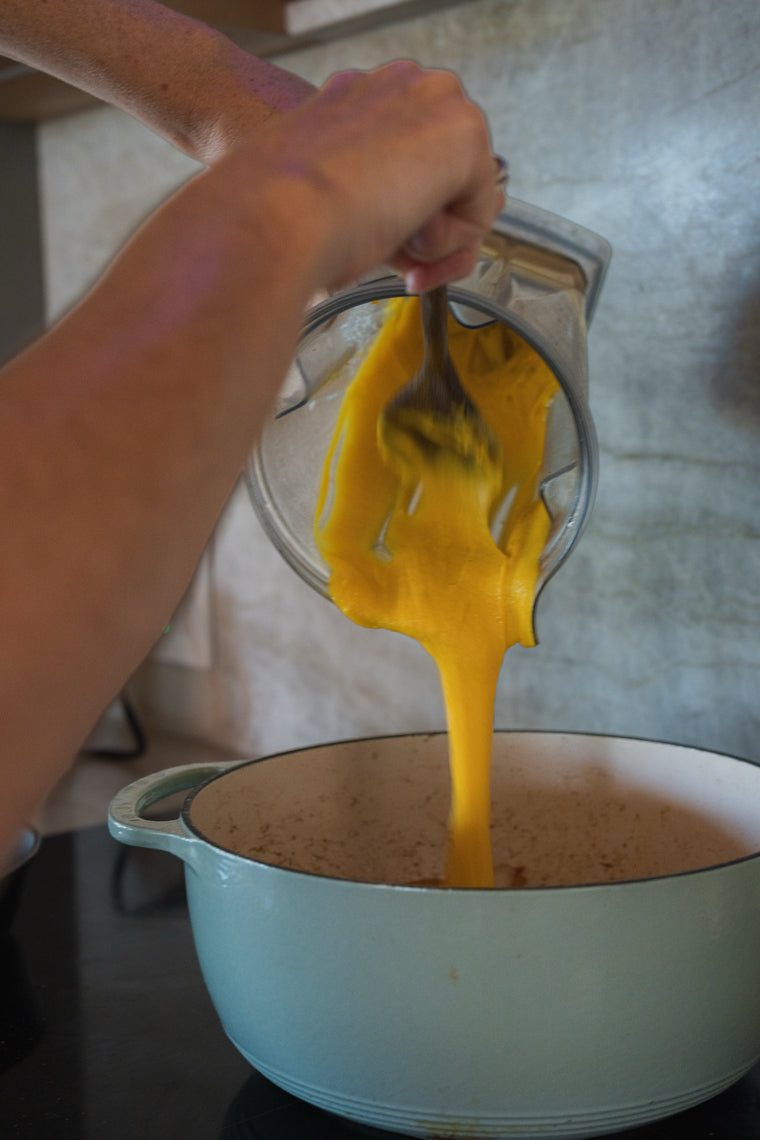 Blended pumpkin and coconut sauce being poured into a pot of bloomed spices