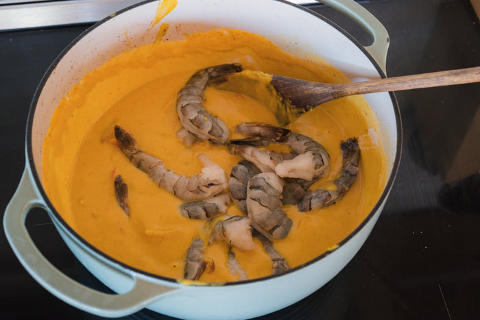 Raw black tiger shrimp being slipped into the pumpkin coconut sauce