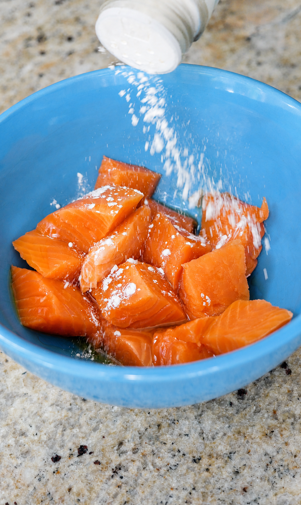 Raw steelhead cut into cubes in a blue bowl, being seasoned