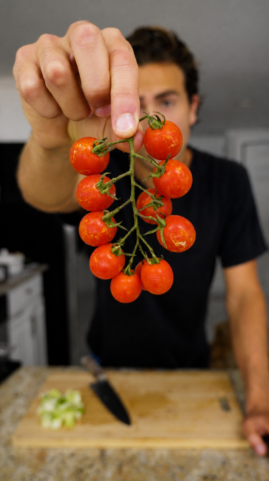 Holding a vine of cherry tomatoes above a cutting board of sliced cucumber