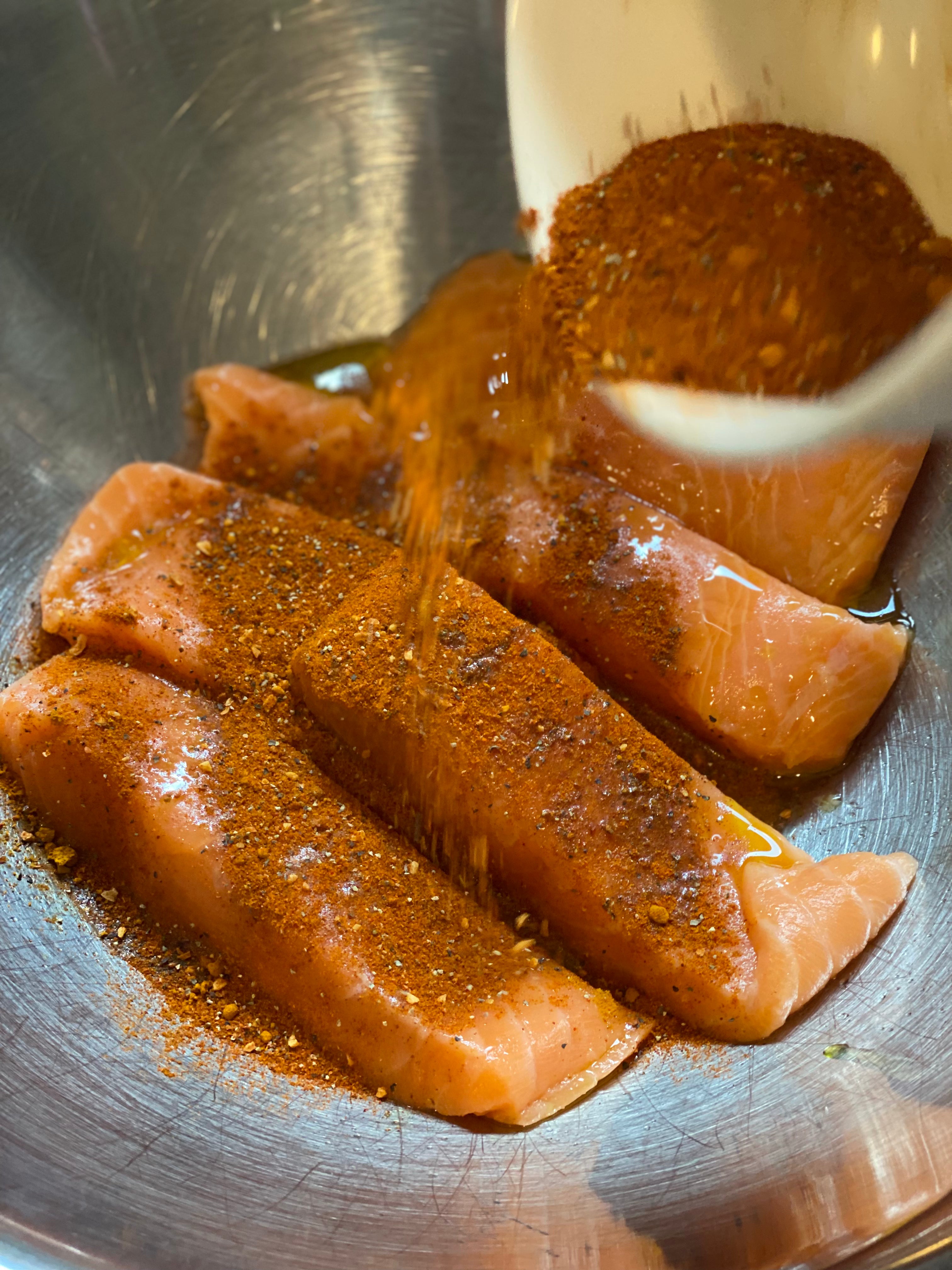 Peri-peri seasoning blend being poured over Seatopia salmon portions in a mixing bowl