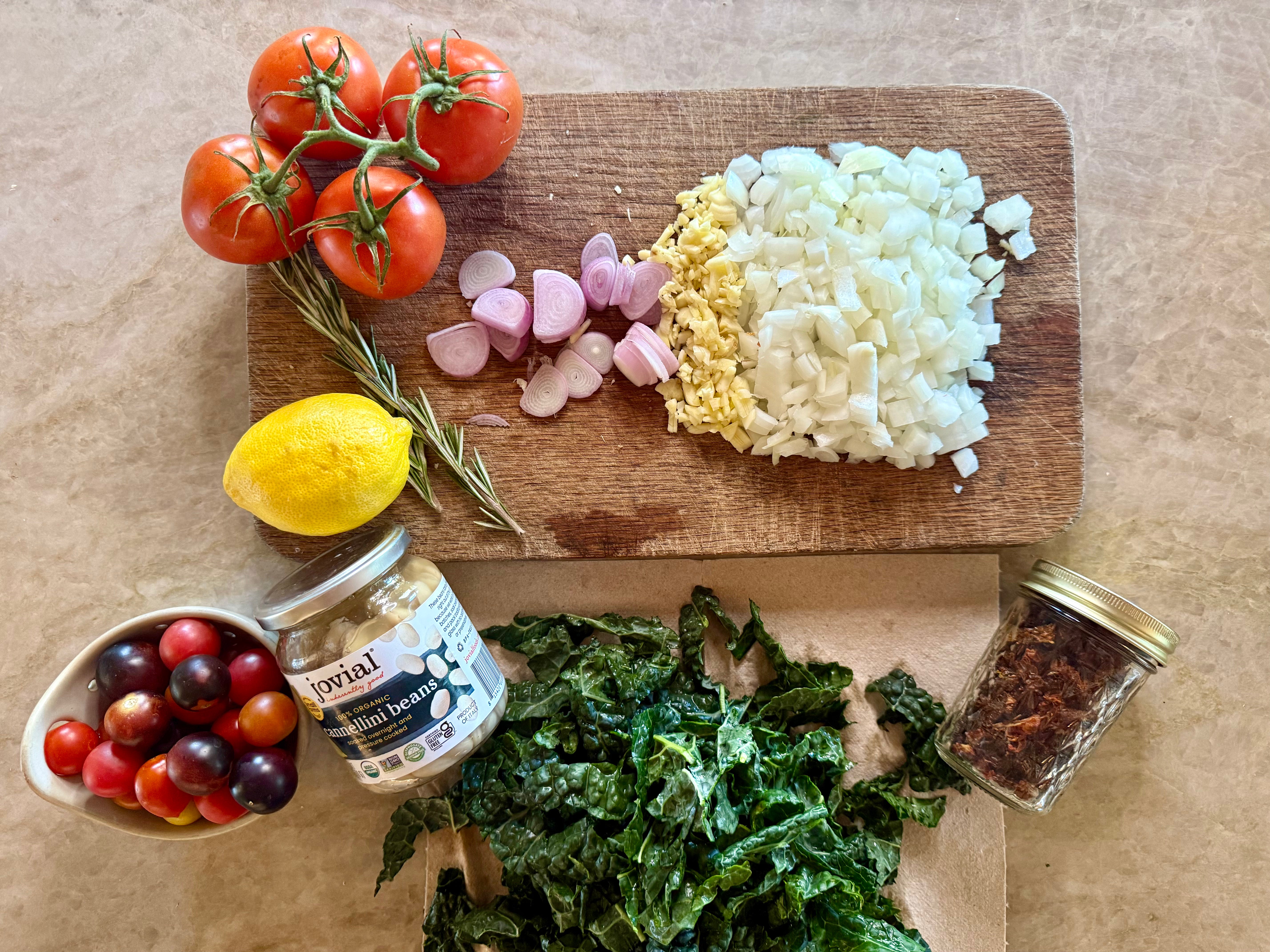 Prep board with chopped shallot, garlic, herbs, lemon and cannellini beans before the skillet goes on