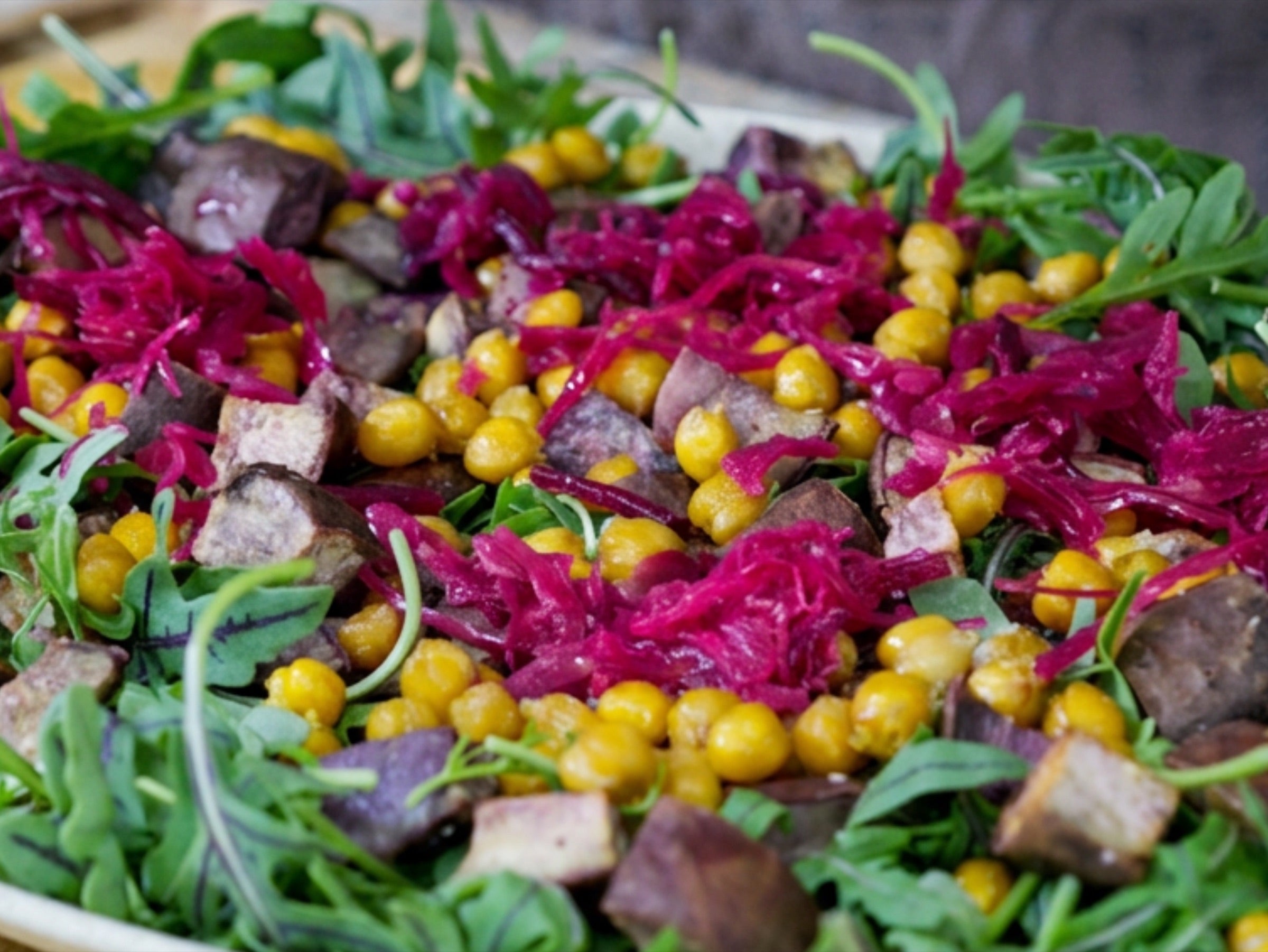 The salad base on a platter: wild arugula layered with roasted Okinawan sweet potato, crispy chickpeas, purple sauerkraut and broccoli sprouts