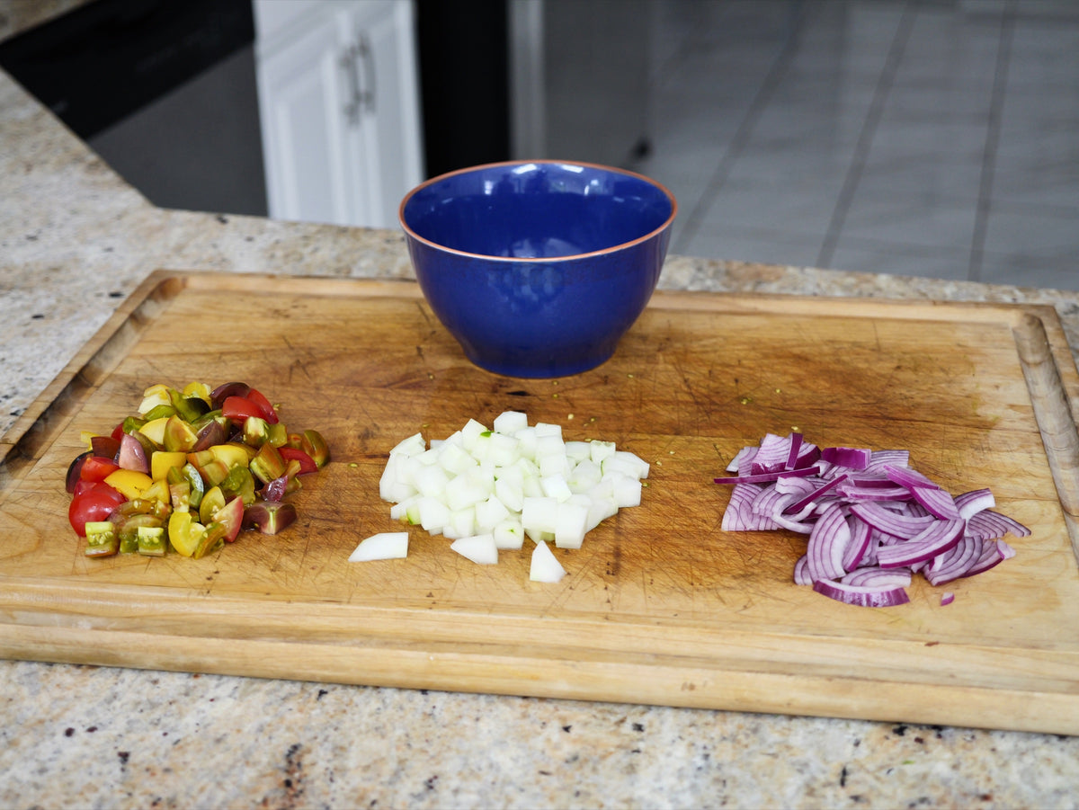 Chopped heirloom cherry tomatoes, diced cucumber and thinly sliced red onion in piles on a wooden cutting board