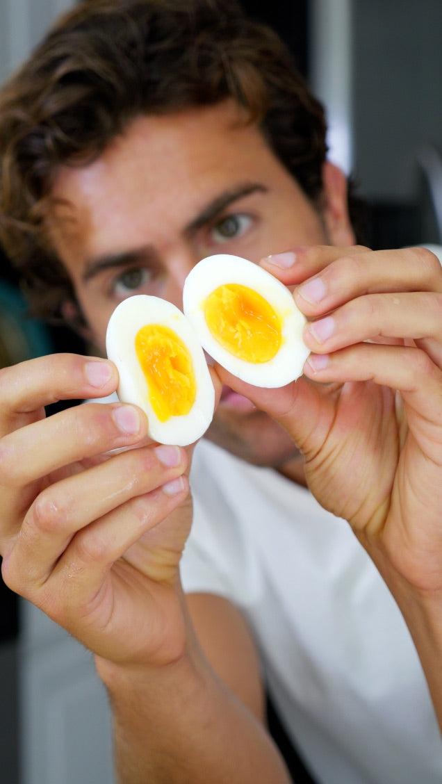 A soft-boiled pasture-raised egg held up and split in half, showing the jammy orange yolk