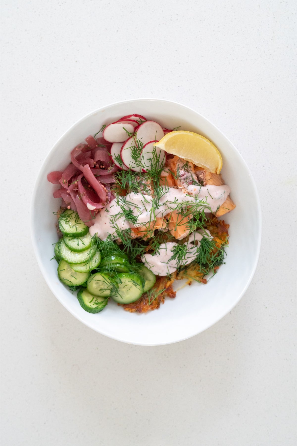 Finished salmon rösti bowl topped with fresh dill, pickled red onion and a lemon wedge
