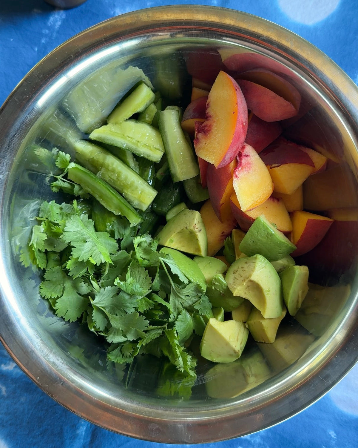 Smashed cucumber, sliced peach, diced avocado and a handful of cilantro in a steel mixing bowl, ready to toss