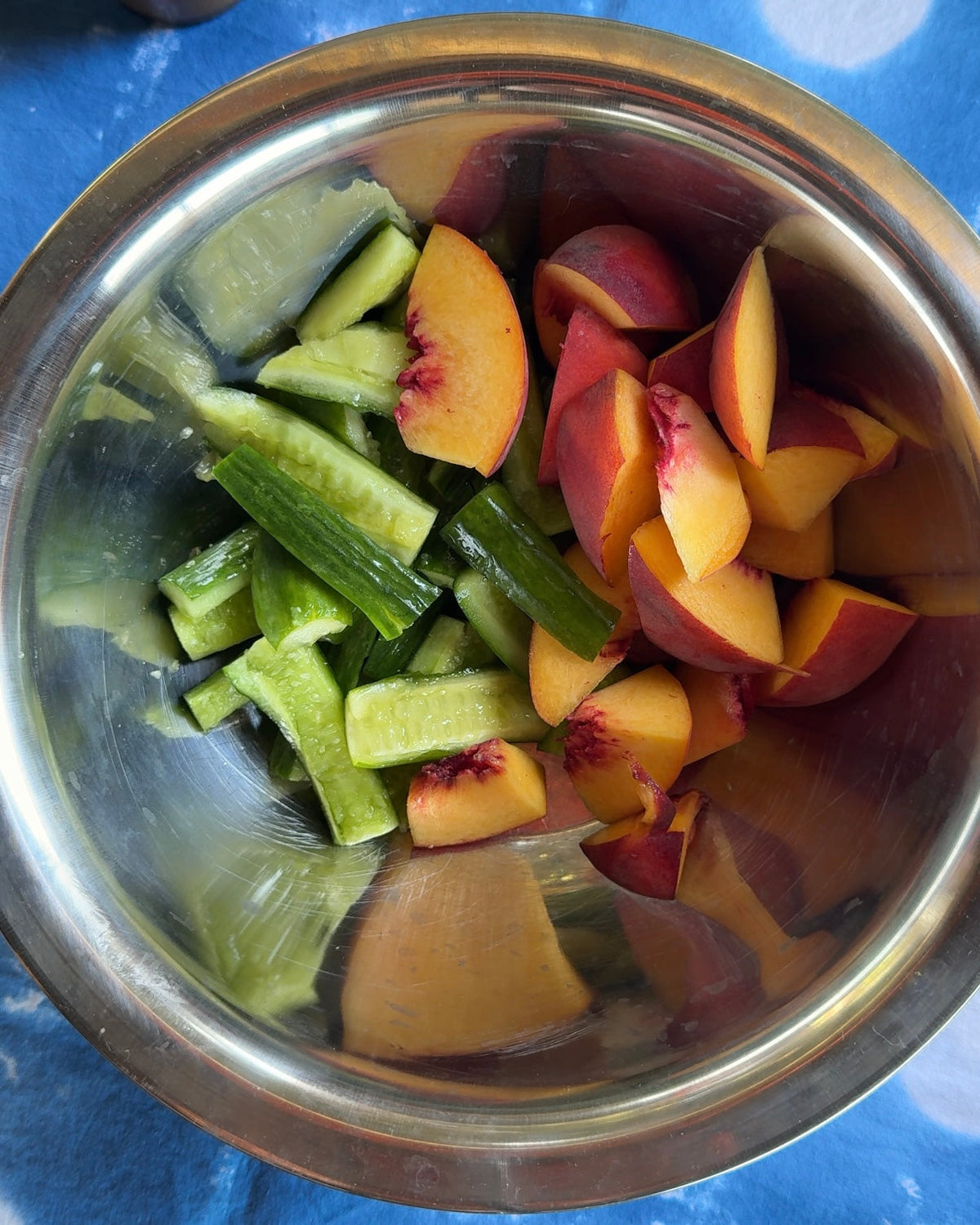 Smashed cucumbers and sliced summer peaches together in a steel mixing bowl