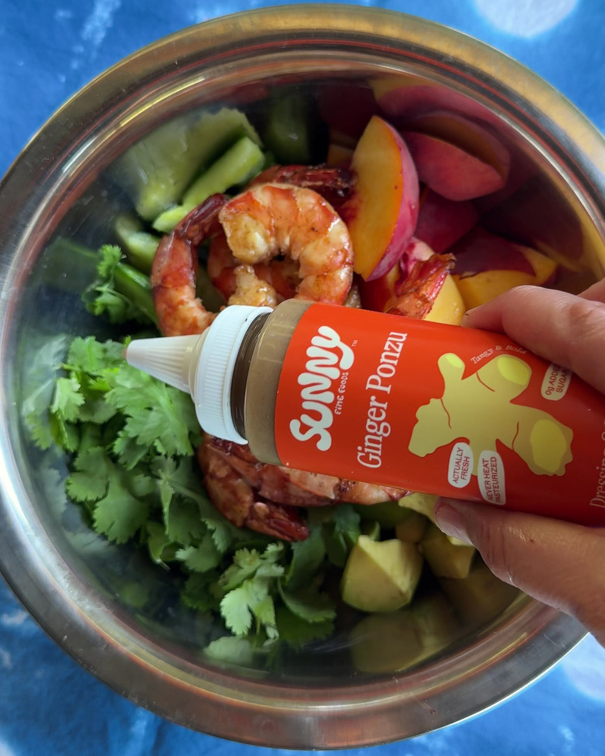 Sunny Fine Foods Ginger Ponzu dressing being drizzled over a bowl of seared shrimp, cucumber, peach, avocado and cilantro