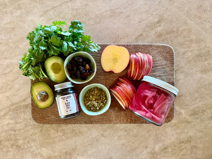 Mise en place on a wooden board: cilantro, avocado, sliced apple, sultana raisins, toasted pepitas, pickled red onions and Urfa pepper